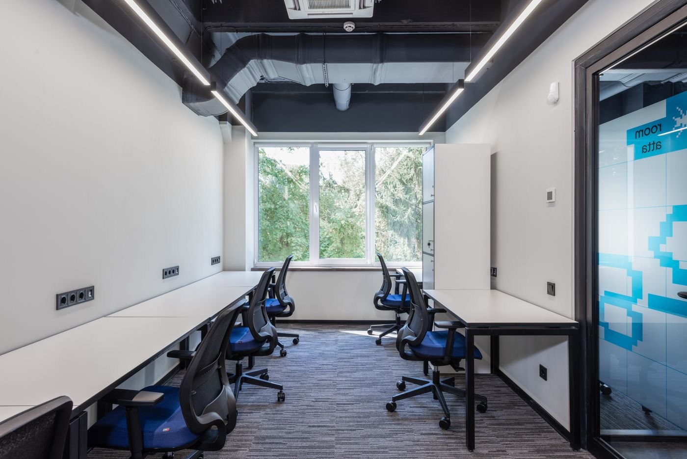 Bright shared workspace with desks, blue chairs and a large window
